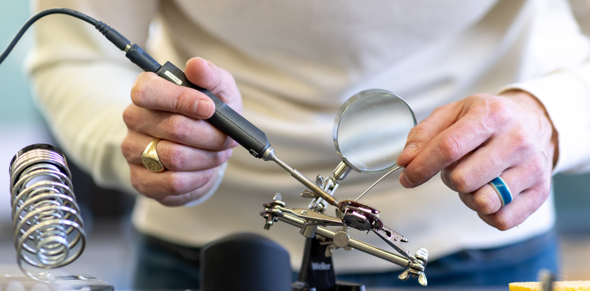 a person soldering an electrical component with a magnifying glass