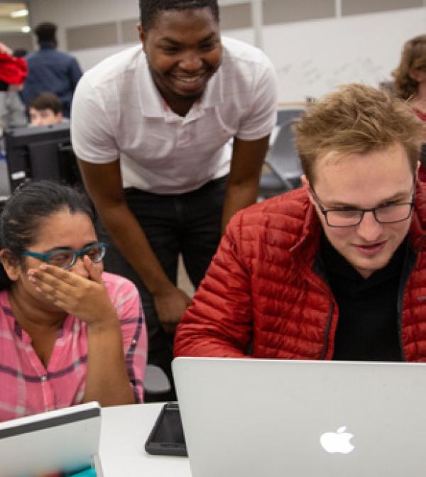 three students smiling about the results they are getting on a laptop